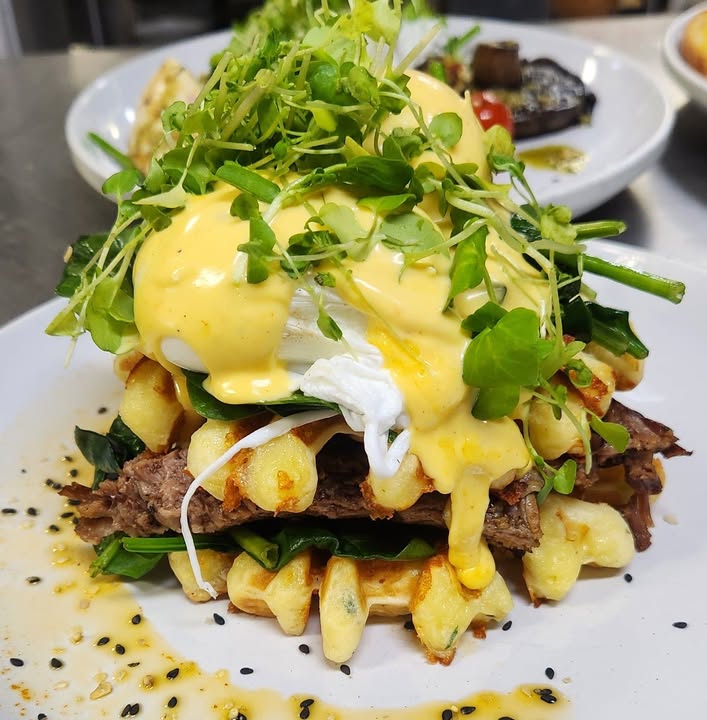 Poached egg and hollandaise over slow-cooked meat and spinach on waffles
